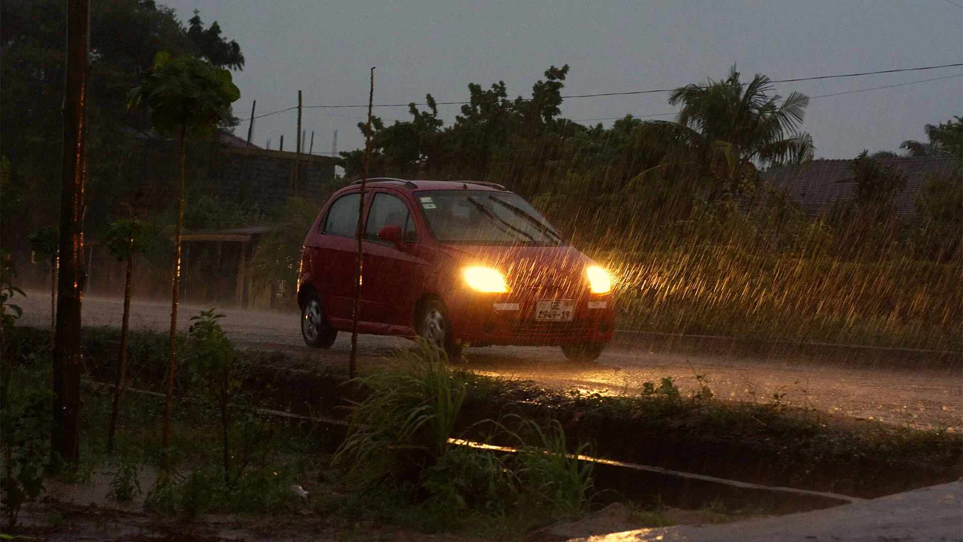 Farol de carro aceso iluminando a pista na chuva