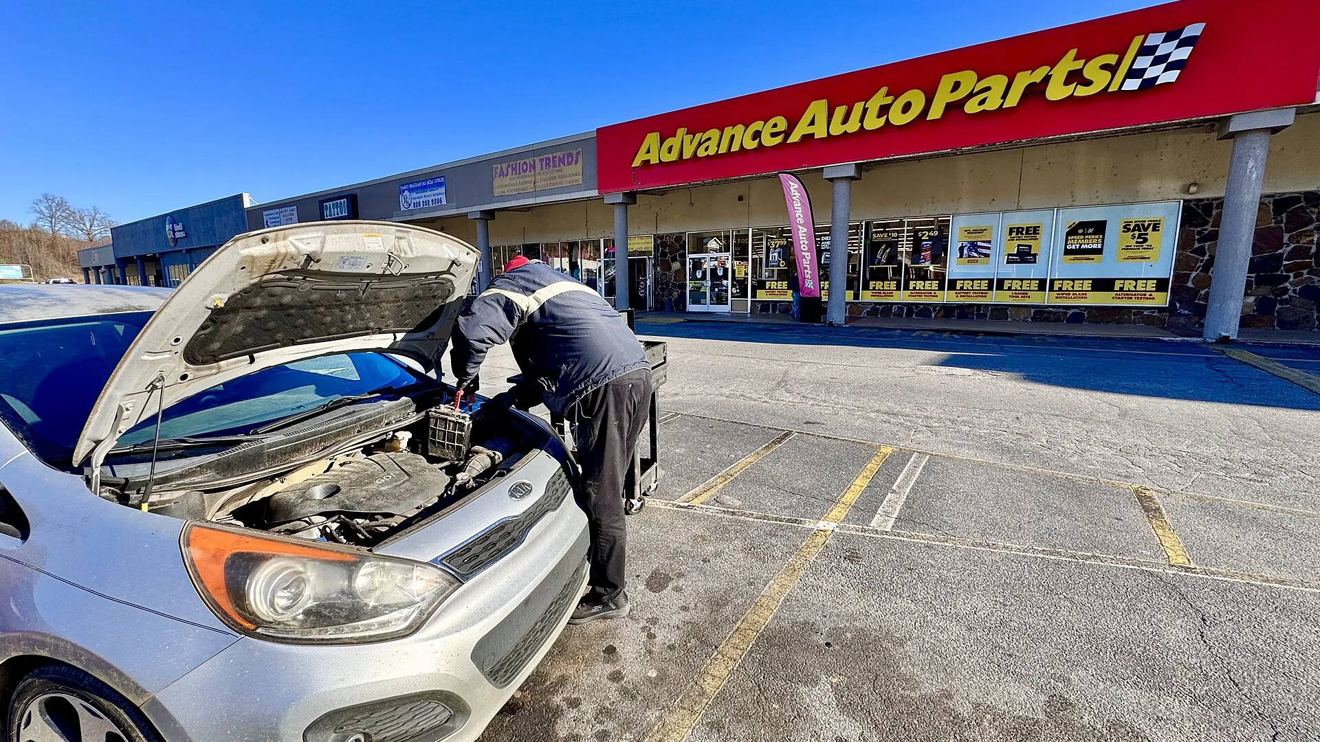 Funcionário de loja de autopeças instalando uma peça no carro do cliente