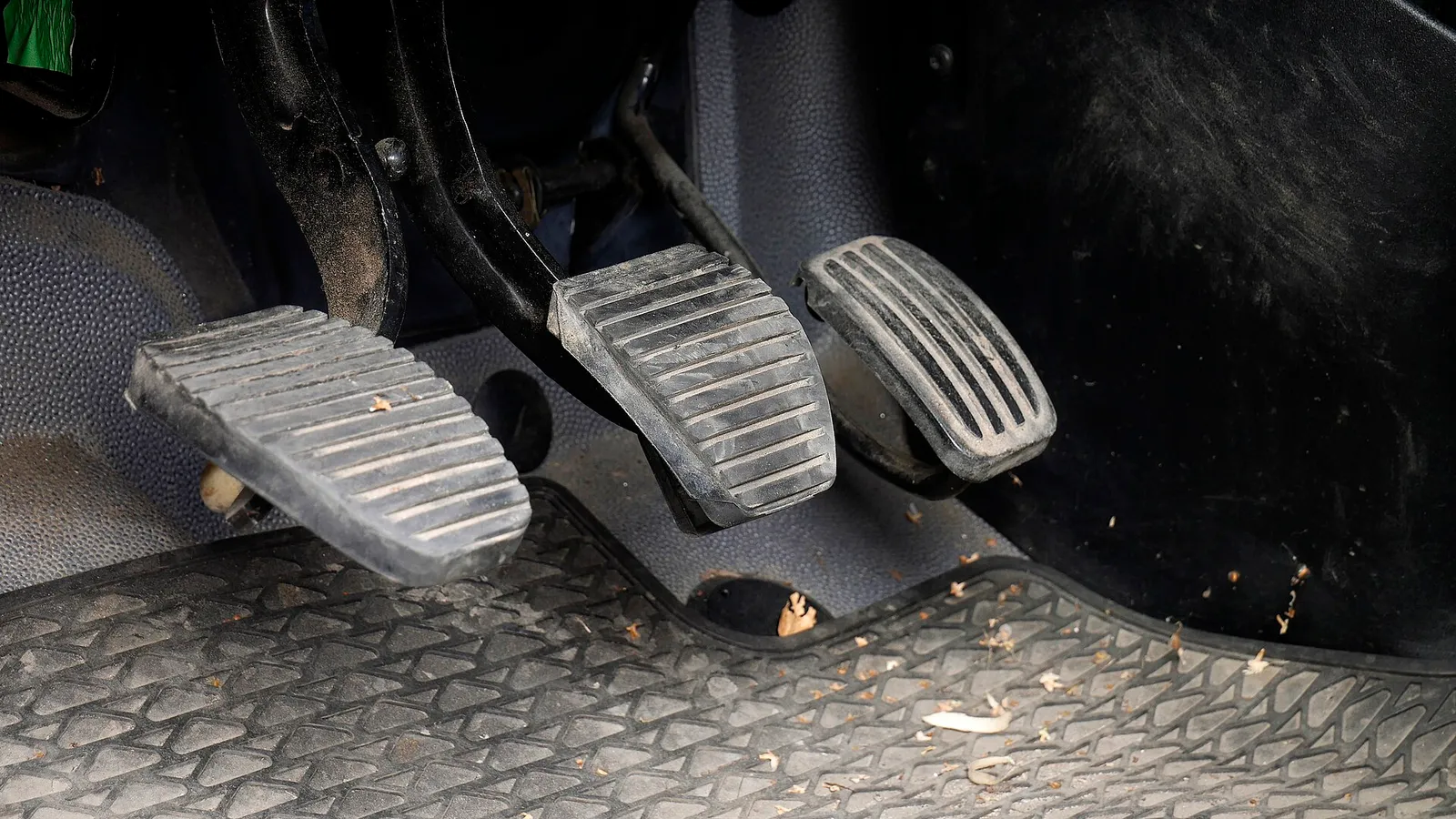 Pedais de um carro vistos de perto no assoalho, junto ao pedal de freio